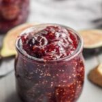 Homemade fig jam in a glass jar next to fresh figs