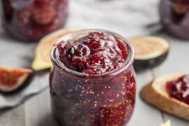 Homemade fig jam in a glass jar next to fresh figs