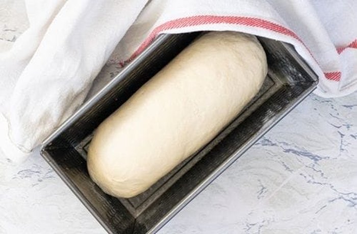 Rolled sandwich bread dough placed seam side down in a buttered loaf pan