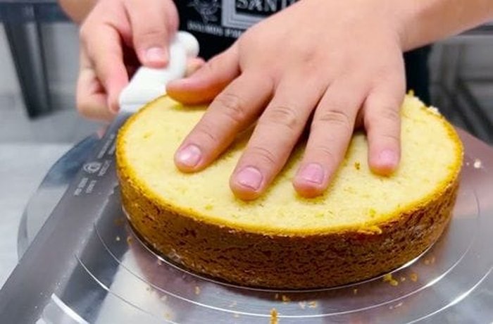 Slicing a Chilean sponge cake horizontally into layers for a torta