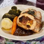 Roast turkey breast stuffed with ham and apples, sliced and served with sauce